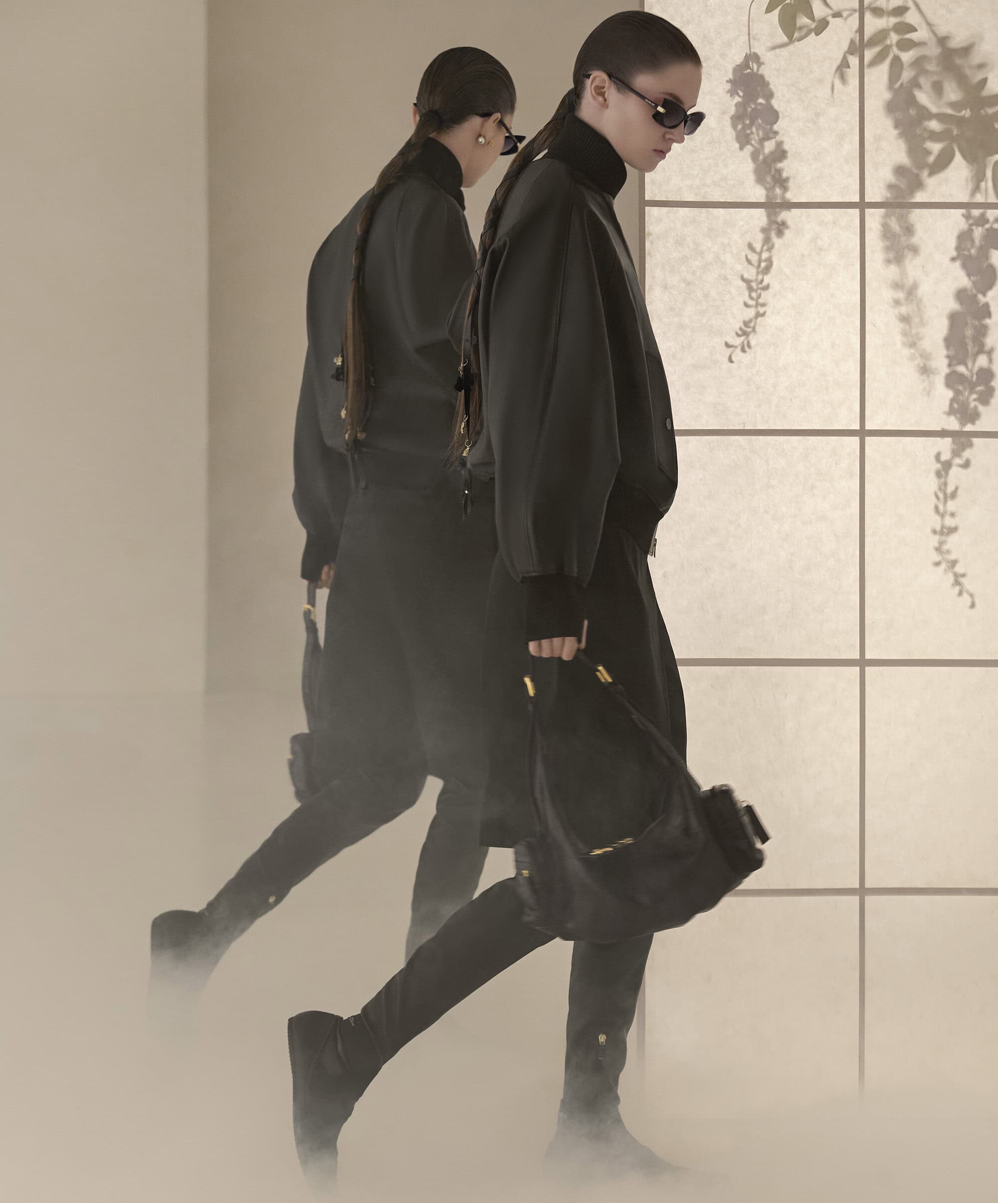 Model in dark clothing and sunglasses holding a black handbag walking past a shoji screen