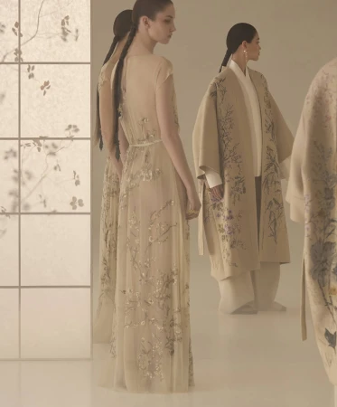 Models in embroidered dresses and coats posing in a muted studio setting with a backlit shoji screen panel