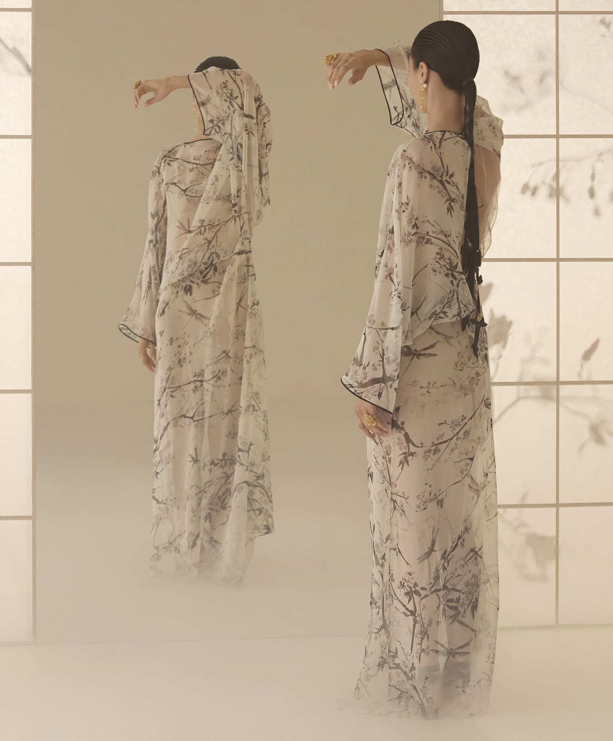 Model in printed sheer floral dress posing before a large mirror reflecting her back view, captured for Dior campaign.