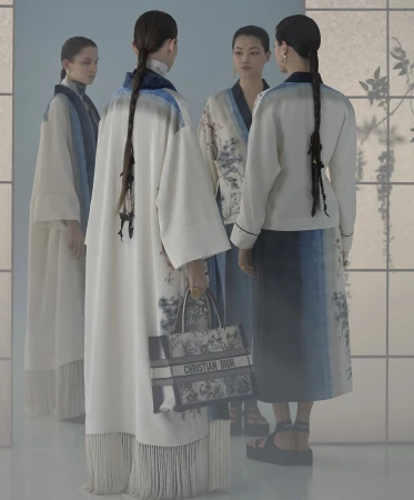 Four female models wearing patterned cream and blue garments holding a Christian Dior tote bag in a studio setting