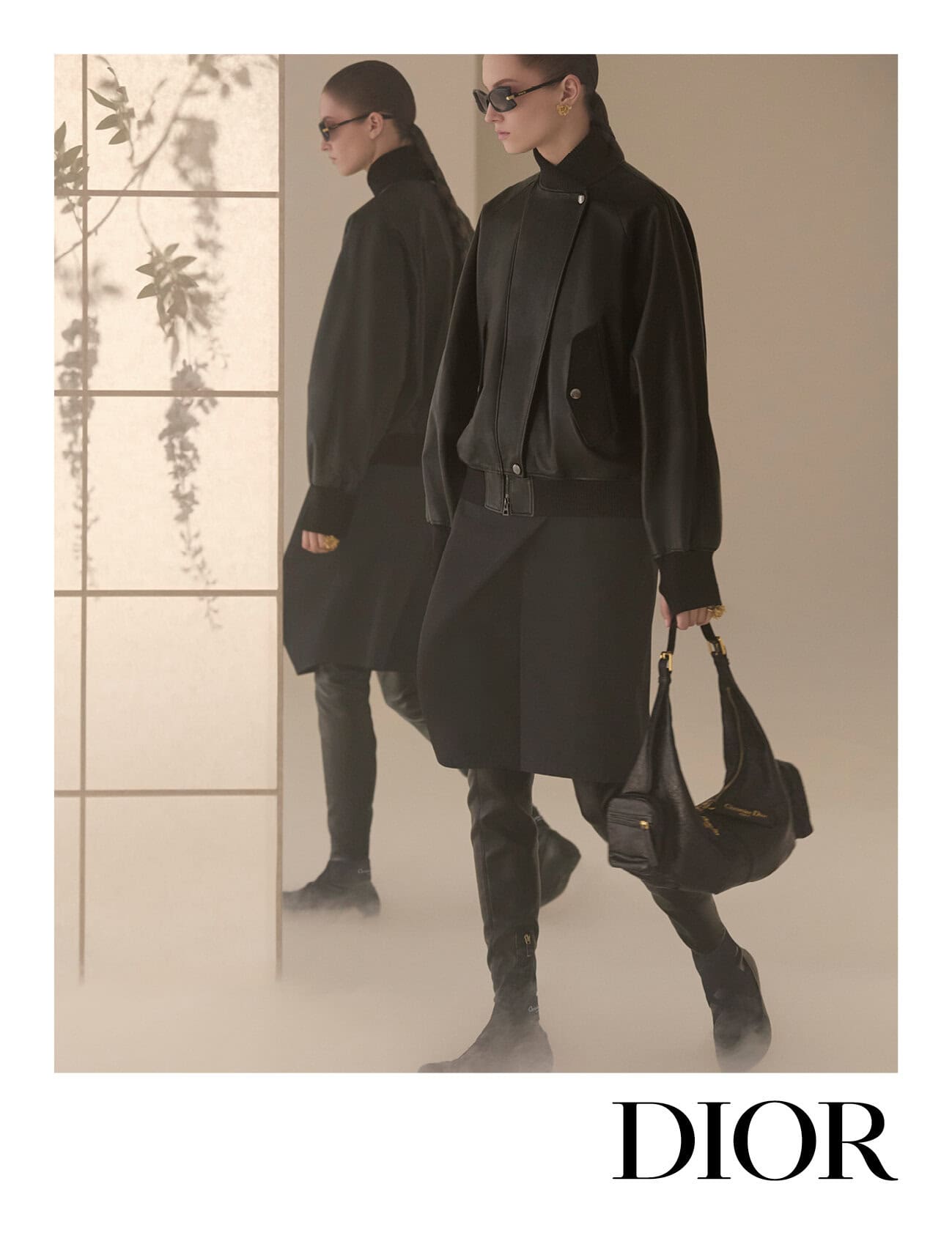 Two female models wearing black outfits and dark sunglasses walk past a translucent shoji screen in a studio ad campaign for Dior.