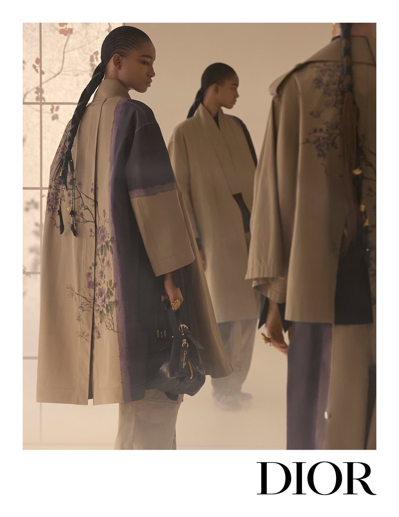 Three models wearing patterned coats and holding handbags in front of a window pane backdrop for Dior Fall 2025.