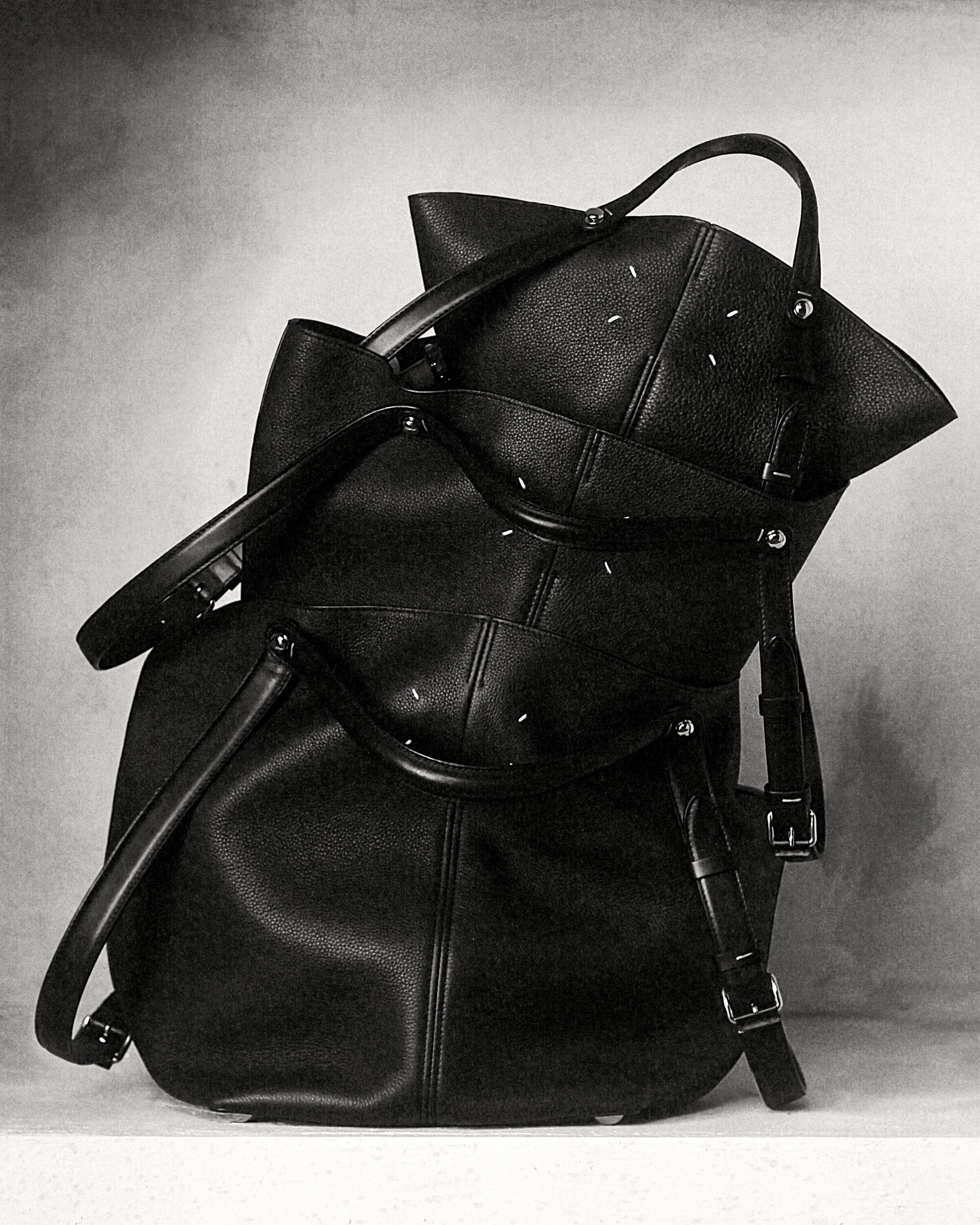 Black leather designer handbags stacked on a textured studio backdrop for Maison Margiela ad campaign
