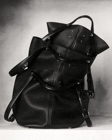 Black leather designer handbags stacked on a textured studio backdrop for Maison Margiela ad campaign
