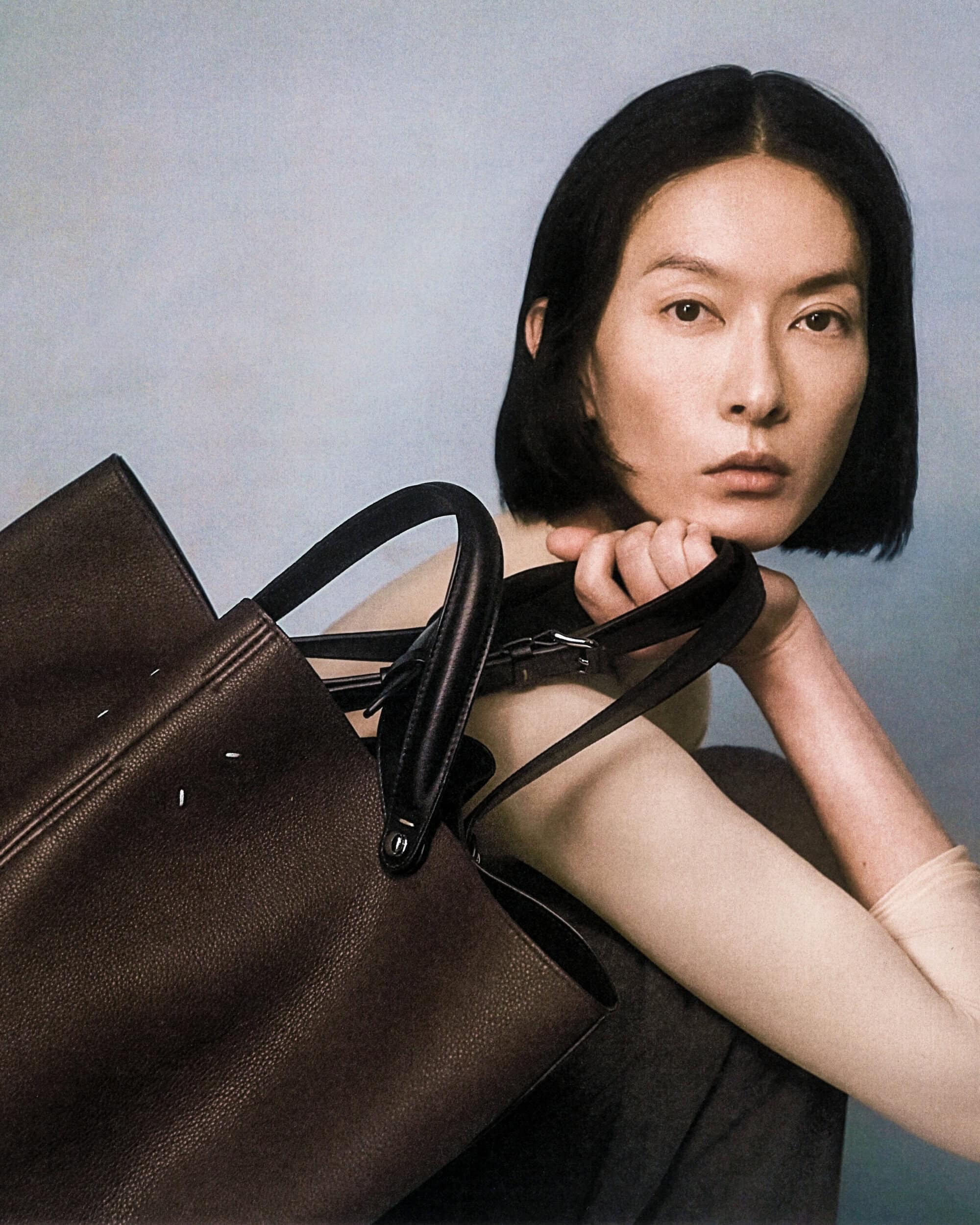 Woman with short black hair holding a dark brown leather tote bag for Maison Margiela Spring 2025 campaign