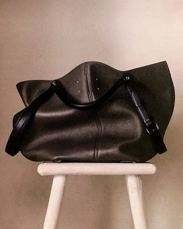 Maison Margiela leather handbag resting on top of a white wooden stool against a neutral wall