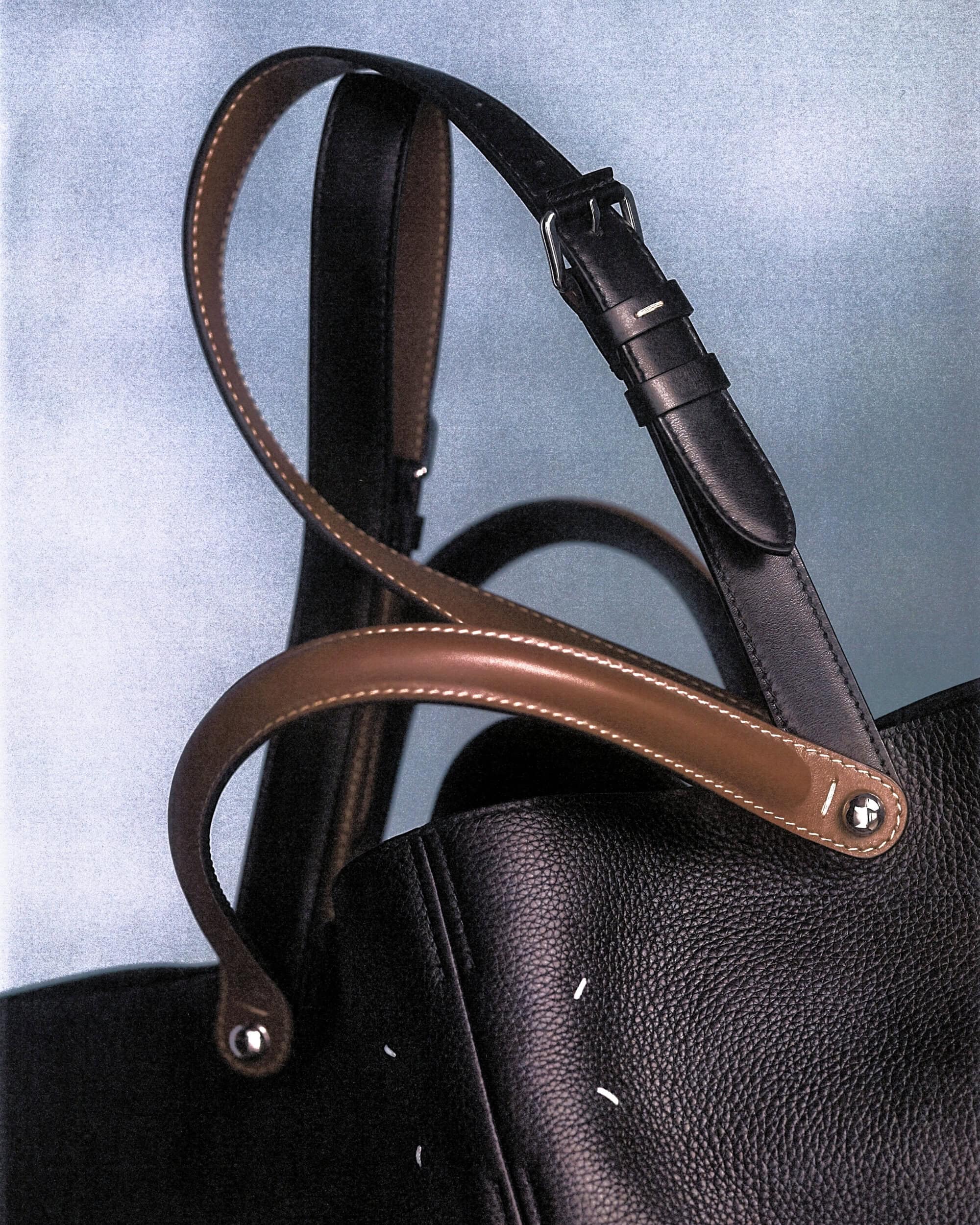 Close up of Maison Margiela leather tote bag with contrasting brown handles and black strap against textured backdrop