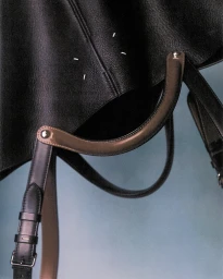 Close up of a black leather handbag with brown handles against a gradient blue background
