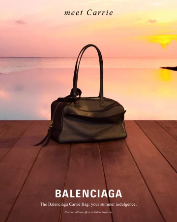 Balenciaga black leather shoulder bag resting on a wooden dock with an ocean sunset in the background.