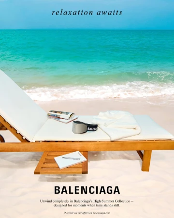 Wooden sun lounger on a sandy beach with sunglasses, magazines and a folded white towel against a turquoise ocean.