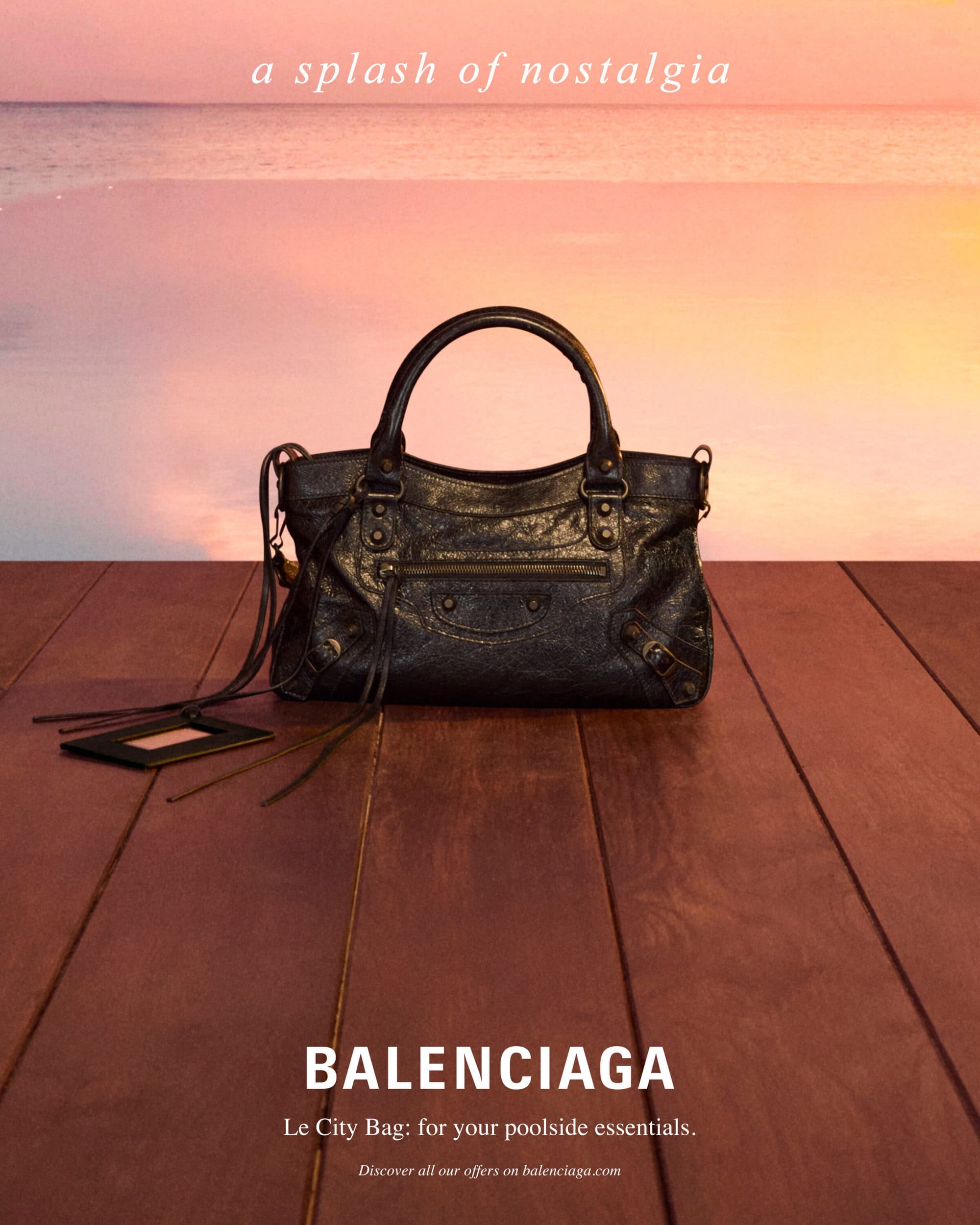 Black leather handbag sitting on a dark wooden deck against a sunset beach backdrop for Balenciaga advertising campaign.