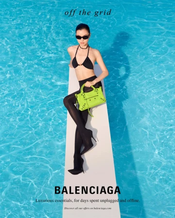 Model wearing black bikini and sunglasses sitting on a diving board holding a bright green handbag over a blue swimming pool