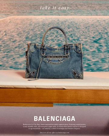 Balenciaga denim handbag resting on a white cushion with a sparkling blue water background