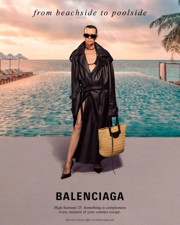Model wearing a black leather trench coat and sunglasses holding a straw tote bag by an outdoor pool at sunset