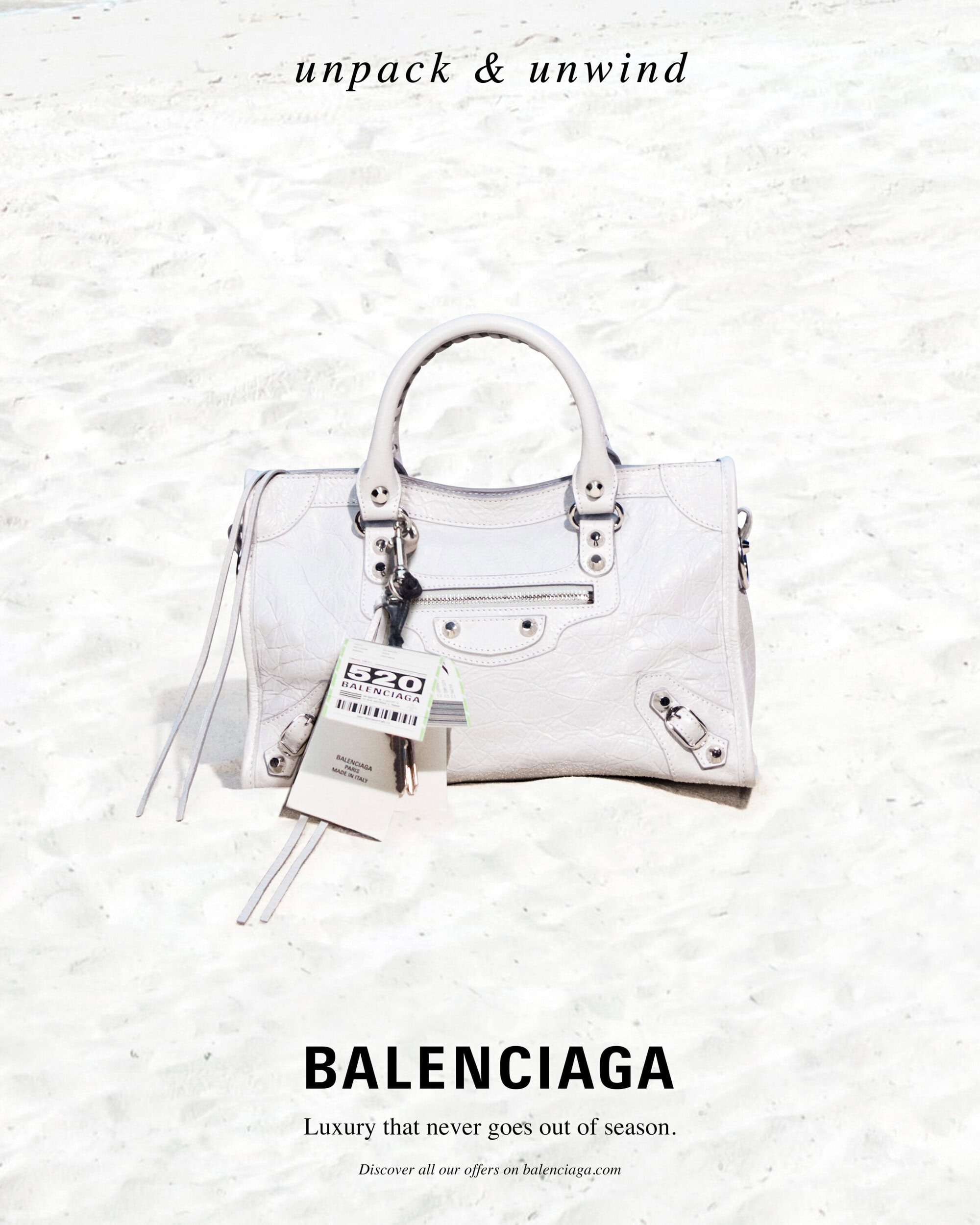White Balenciaga leather handbag placed on a pale sandy beach for a high summer campaign image photographed by Roe Ethridge.