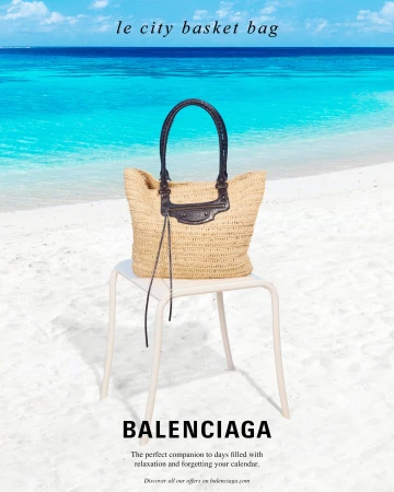 Straw basket bag with dark leather handles resting on a white chair on a sandy beach with bright blue ocean water