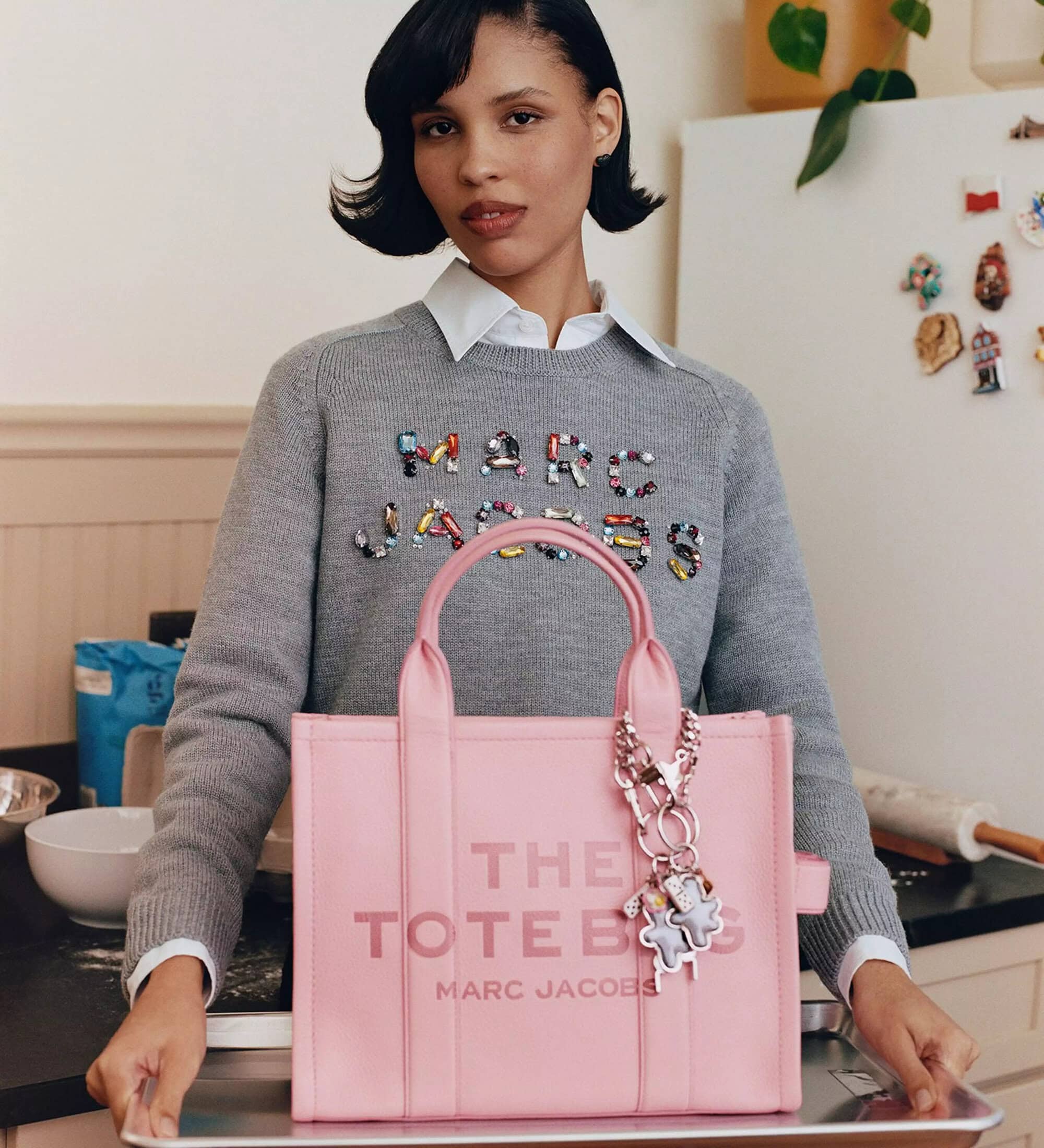 Model Nara Smith holding a pink Marc Jacobs tote bag on a baking sheet in a kitchen setting