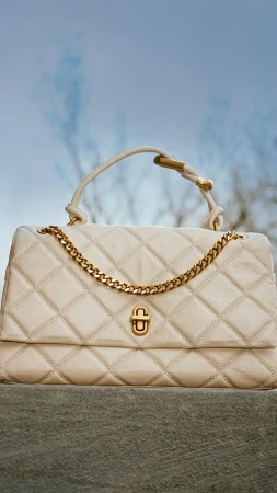 Quilted white leather handbag with gold chain hardware against an outdoor sky background