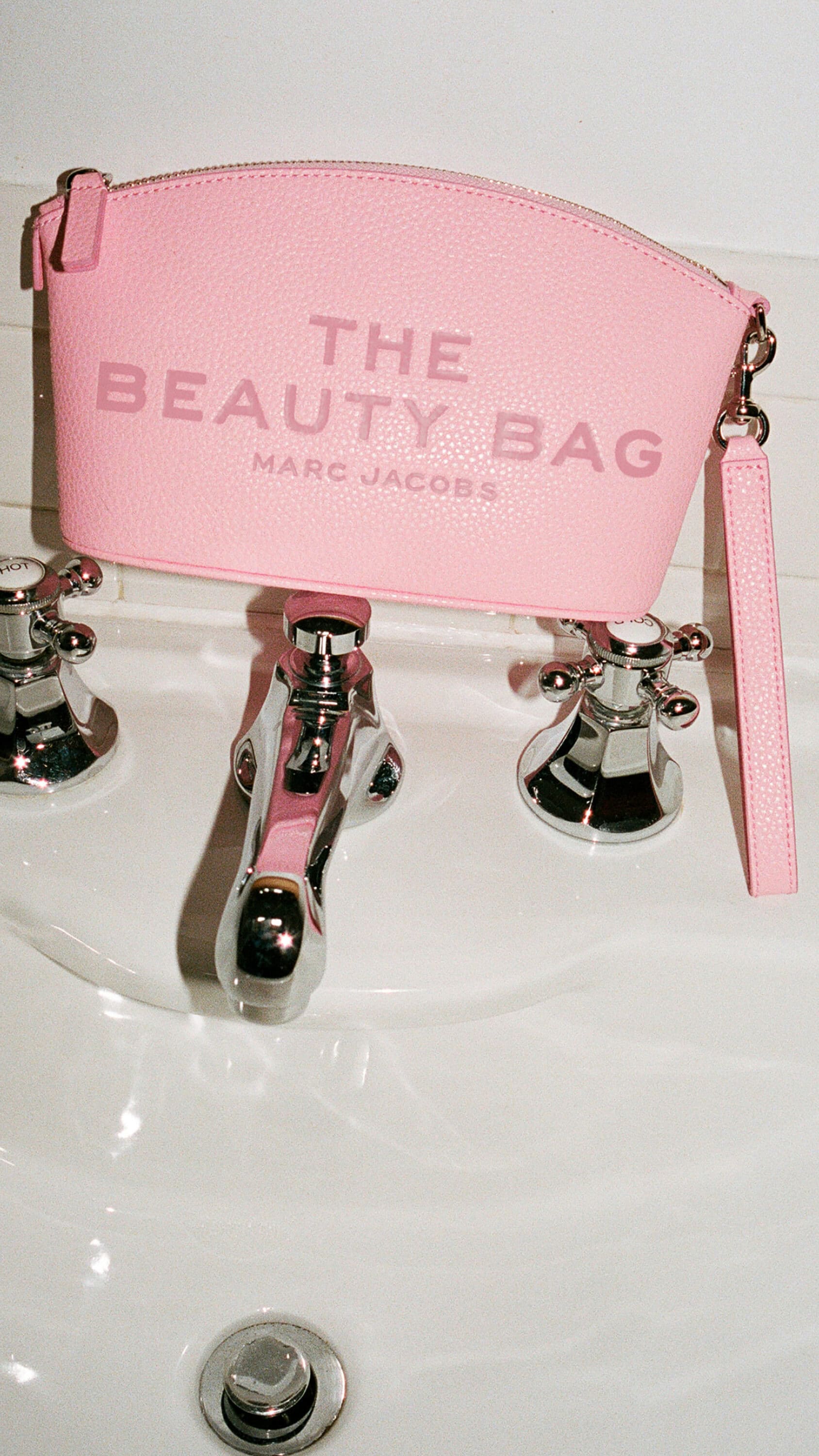Pink Marc Jacobs beauty bag resting on a white bathroom sink faucet for the Mother's Day ad campaign.