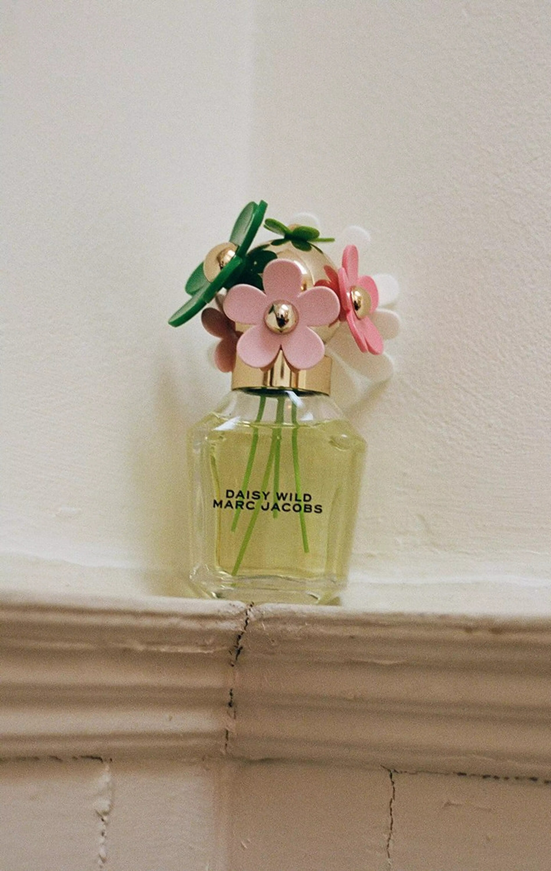 Marc Jacobs Daisy Wild perfume bottle with flower cap resting on a pale painted ledge
