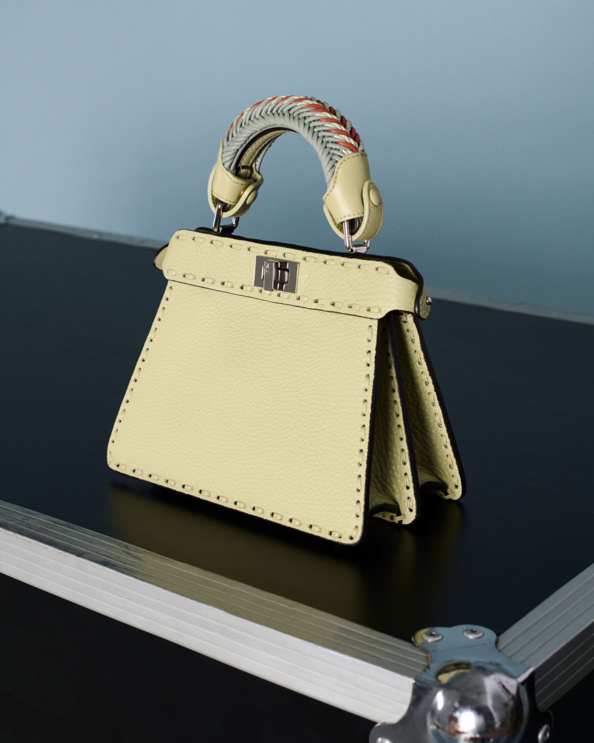 Fendi yellow leather handbag with woven handle resting on a dark flight case surface