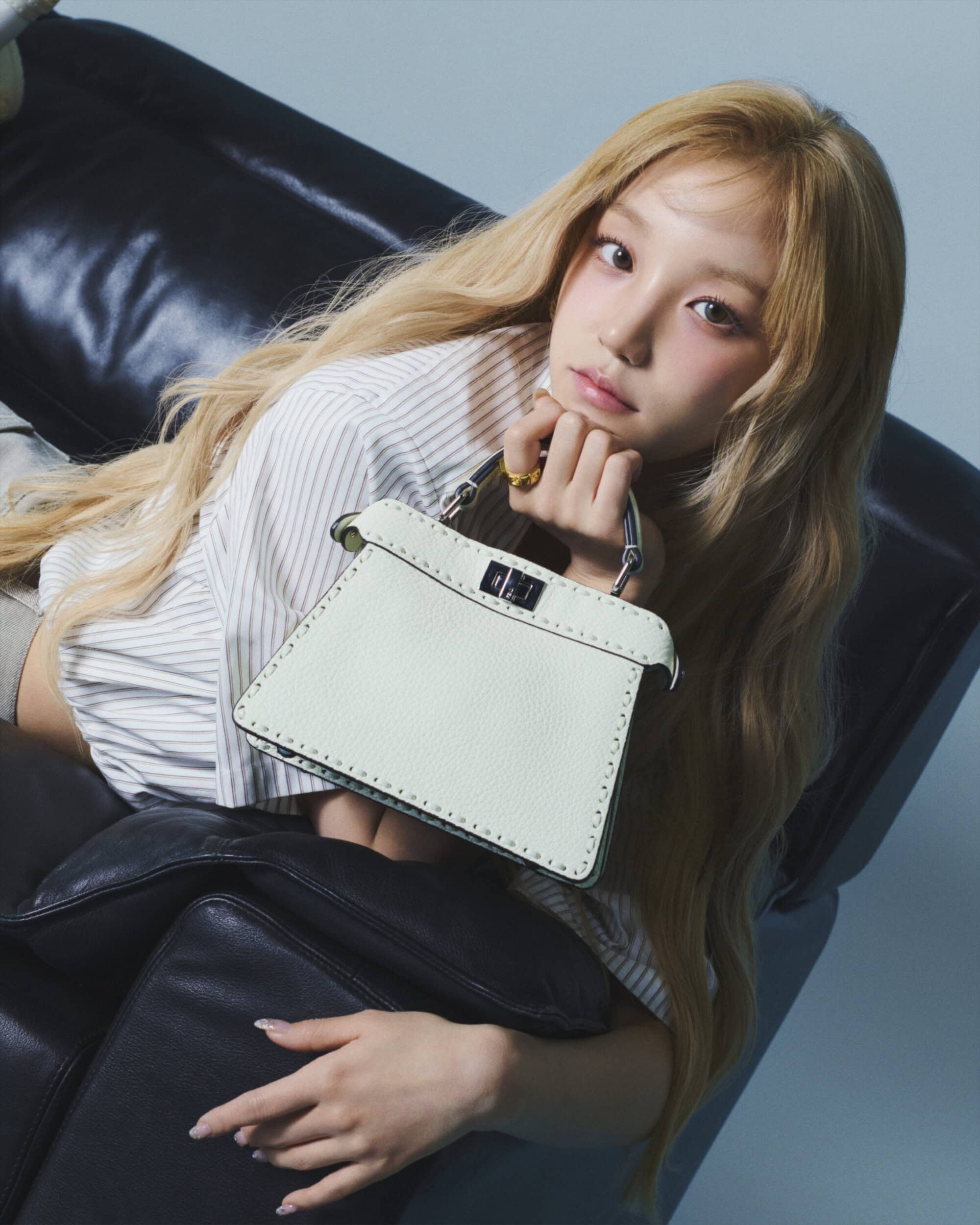 Model Song Yuqi posing with a white Fendi handbag while reclining on a dark leather sofa in an ad campaign.