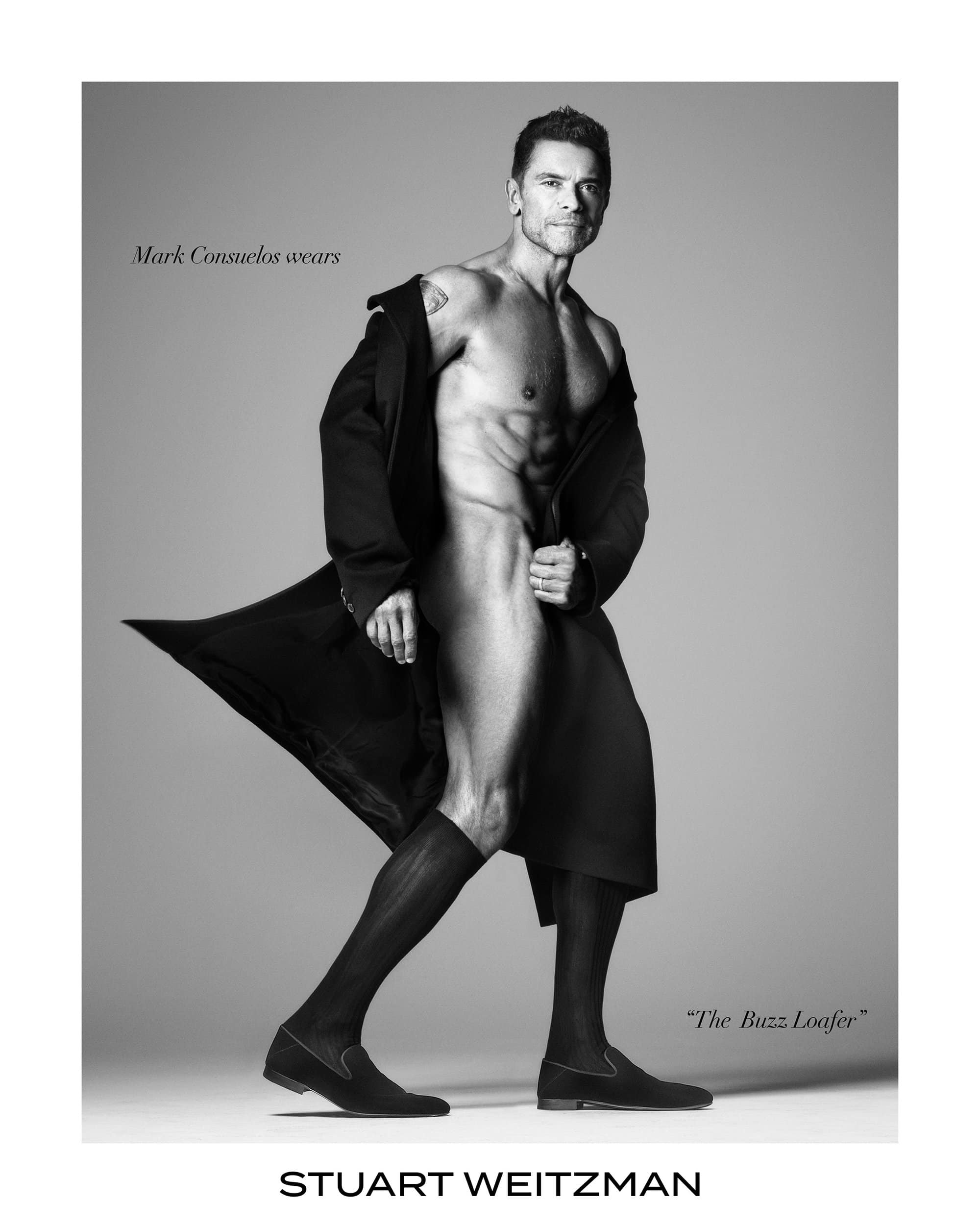 Mark Consuelos wearing loafers and a dark coat against a grey studio backdrop in a Stuart Weitzman campaign image.