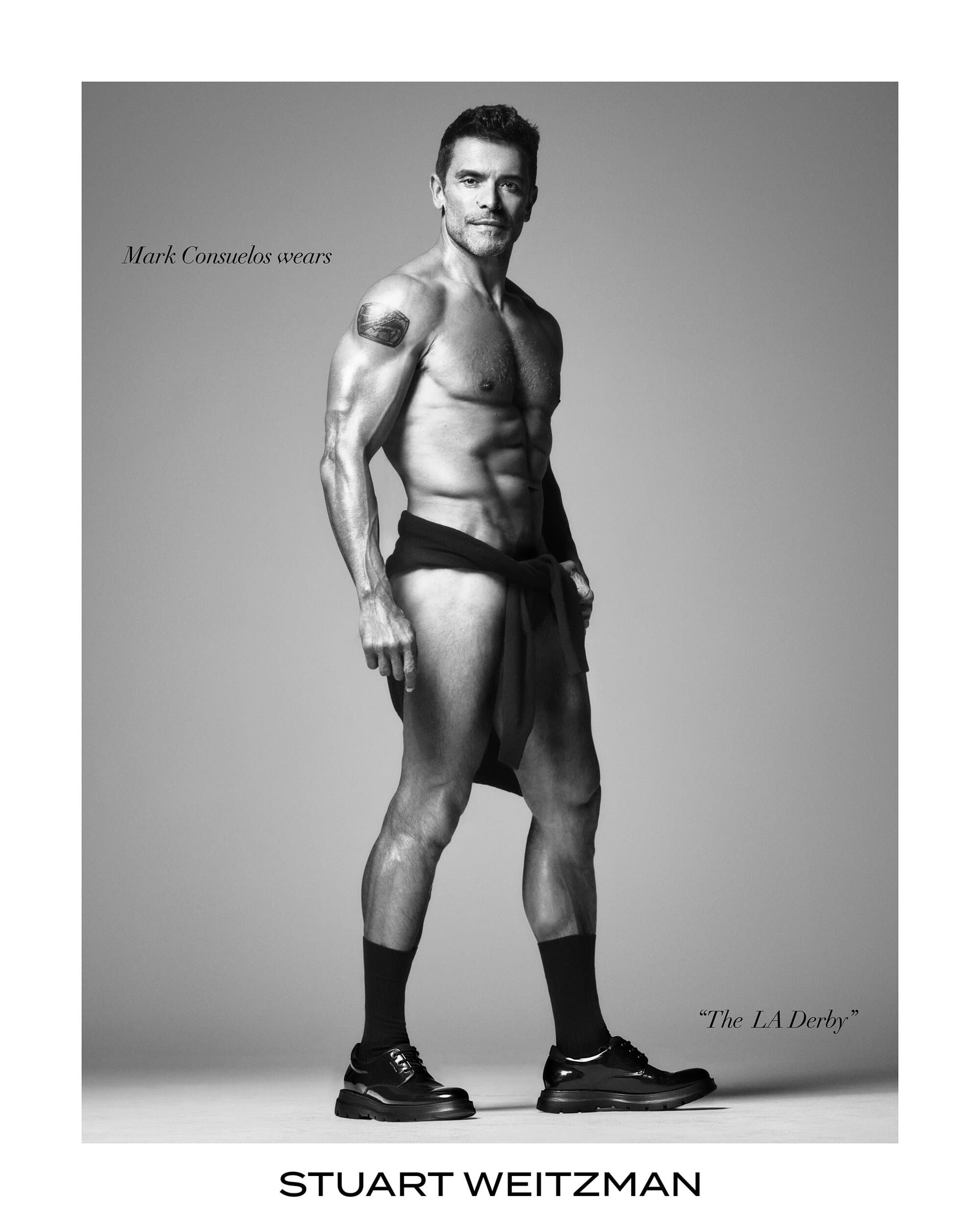 Mark Consuelos wearing black shoes and socks against a grey seamless studio background for Stuart Weitzman campaign
