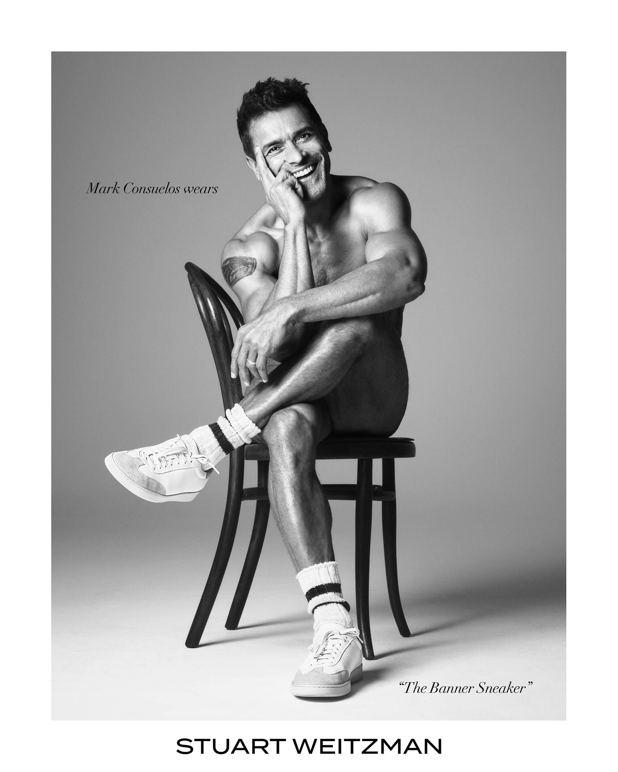 Mark Consuelos seated wearing white sneakers against grey background for Stuart Weitzman campaign
