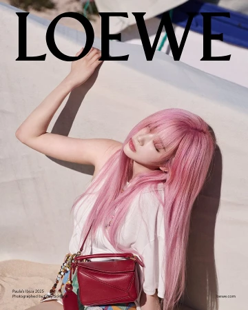 Model with long pink hair wearing a white top and holding a red handbag against a light background