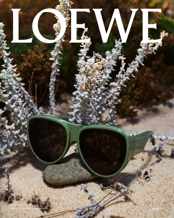 Green sunglasses resting on a stone among sand and pale vegetation for Loewe Paula's Ibiza ad campaign