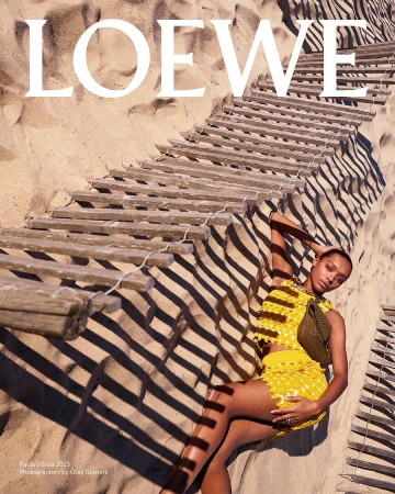 Model wearing yellow textured top and skirt lying on sandy beach beneath wooden boardwalk slats casting shadows.