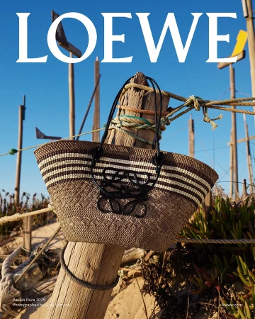 Loewe straw basket bag hanging on a wooden post outdoors against a clear blue sky