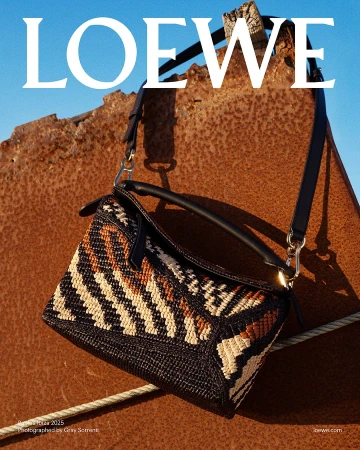 Loewe woven handbag hung against a textured rusty metal surface under a bright blue sky.