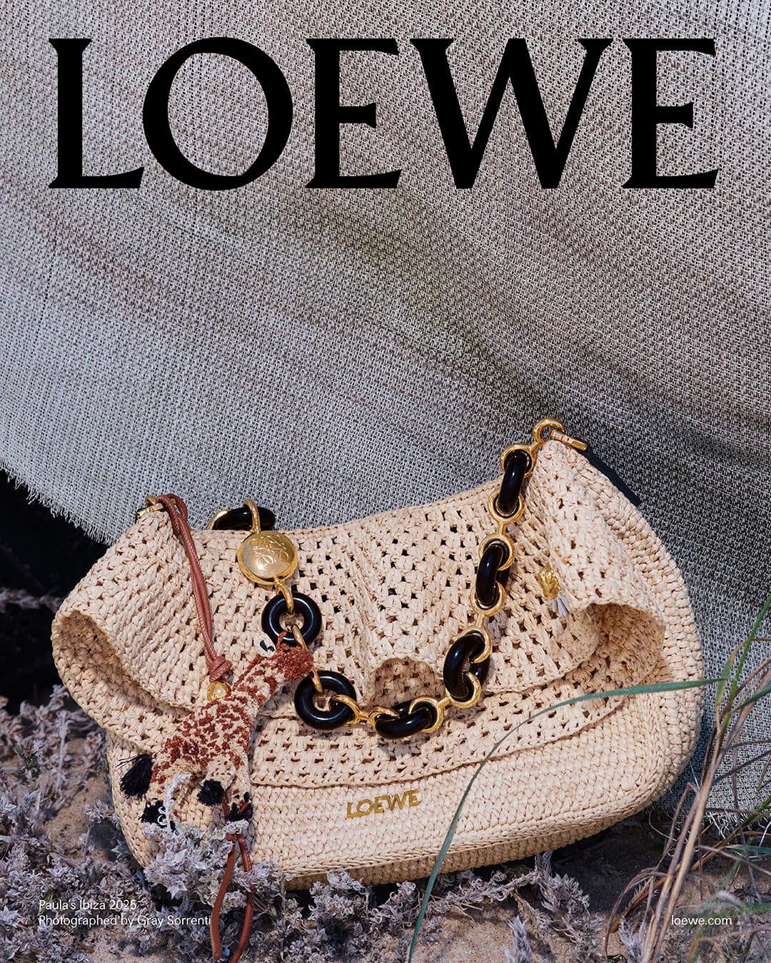 Loewe straw shoulder bag with chain strap and small giraffe charm resting on ground