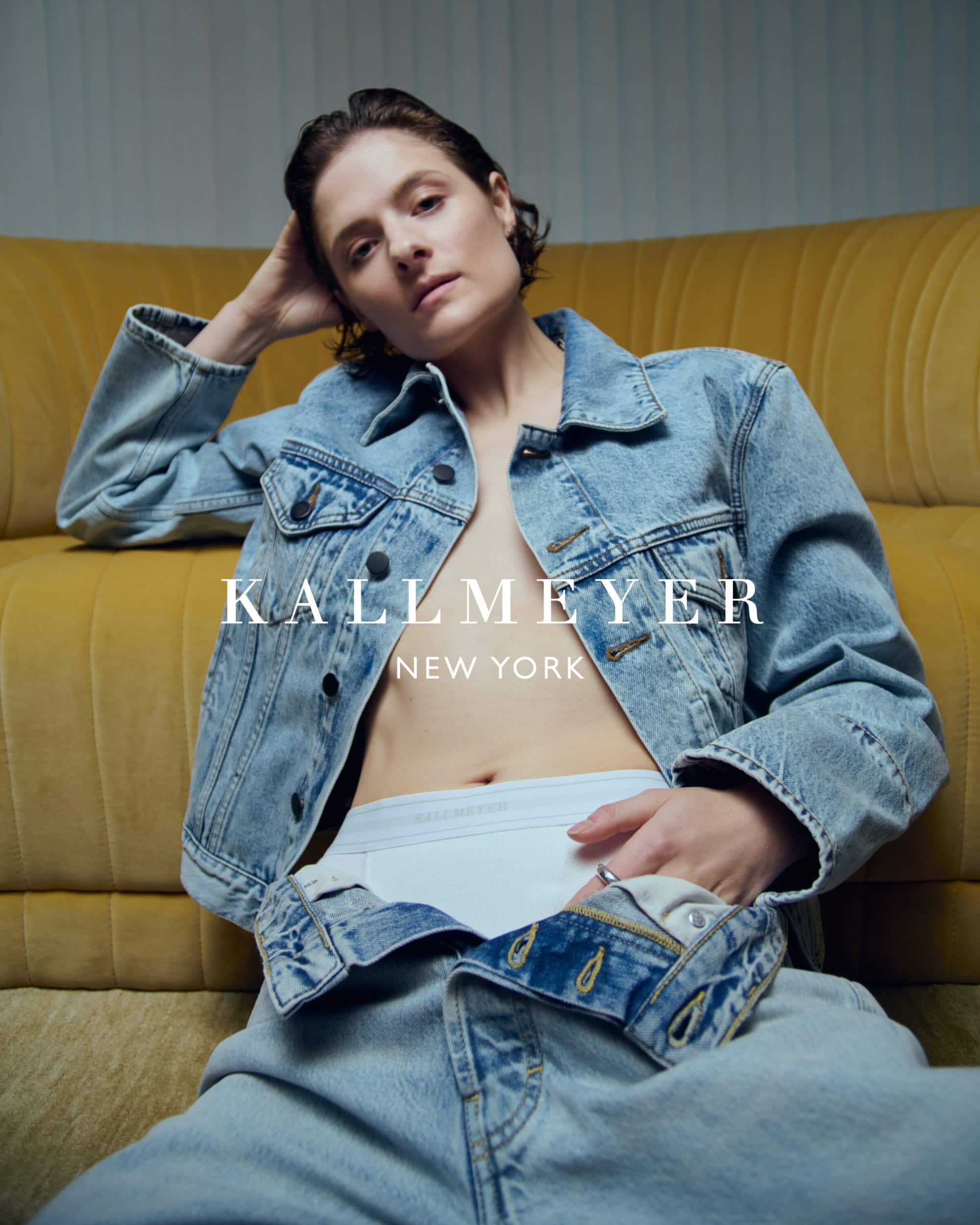 Model wearing a denim jacket and white underwear seated against a yellow sofa for Kallmeyer