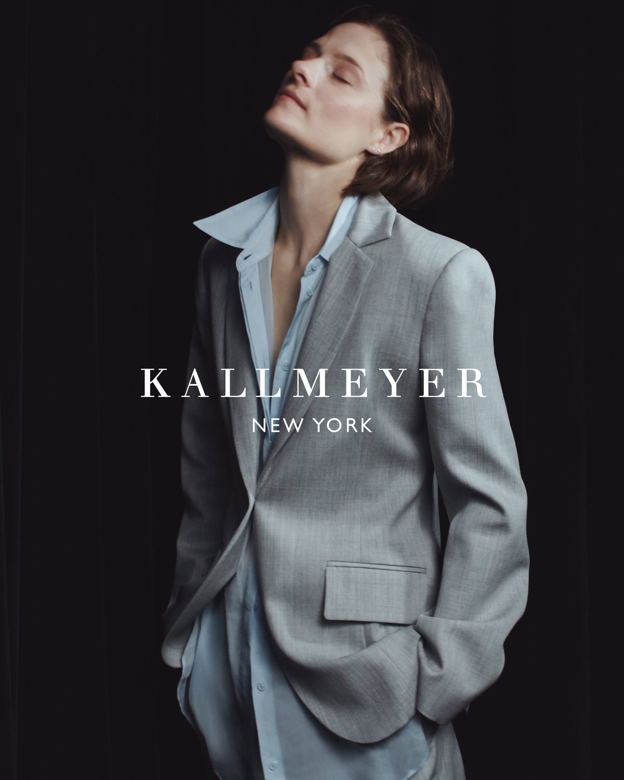 Model in grey blazer and light blue shirt against a dark background for Kallmeyer spring 2025 ad campaign.