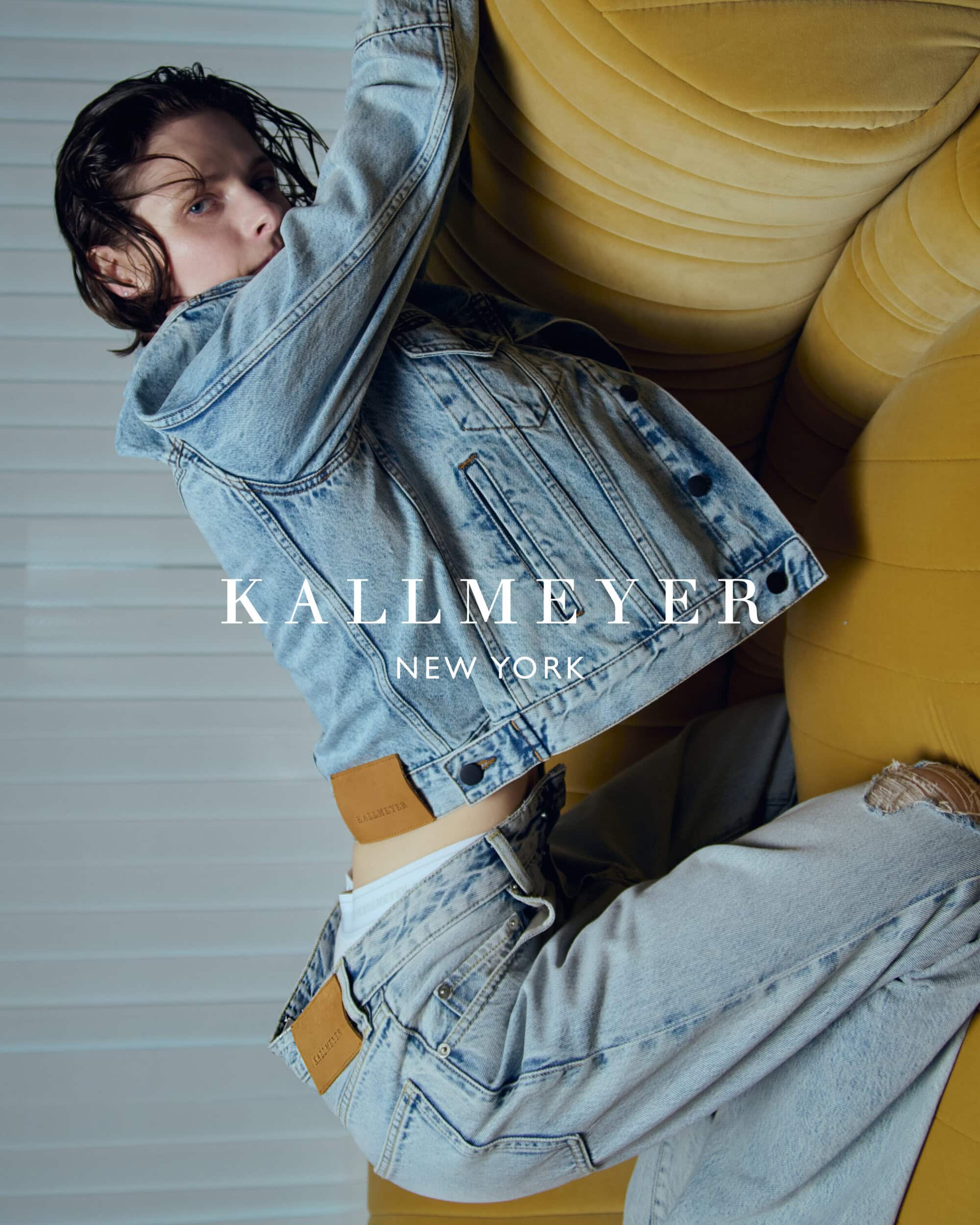 Model wearing a light wash denim jacket and matching jeans leaning against a yellow sofa