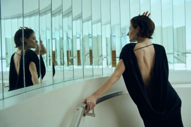 Model Louisa Jacobson in a black dress reflected in vertical mirrors on a staircase for Kallmeyer Spring 2025 ad campaign.