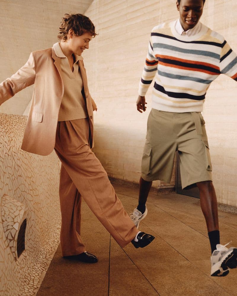 Two models laughing and posing on a textured stone balcony during the Maison Kitsune Spring 2025 ad campaign.
