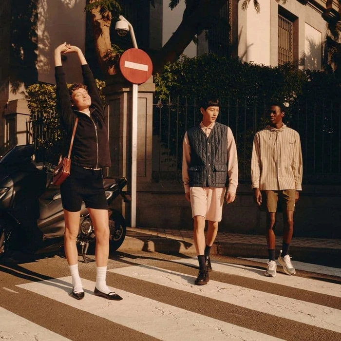 Three models walking across a street crosswalk in sunlight for the Maison Kitsune Spring 2025 campaign.
