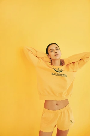 Model Irina Shayk wearing a yellow sweatshirt and matching shorts against a yellow studio backdrop