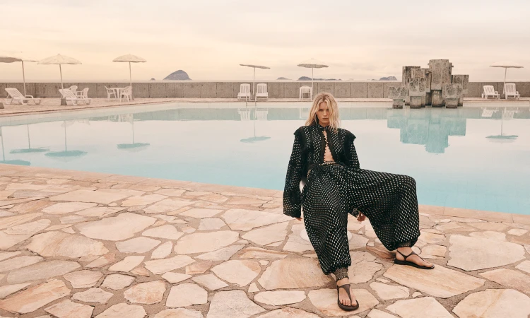 Model Abbey Lee in a black patterned two-piece outfit seated by a poolside terrace for Zimmermann Swim 2025 campaign.