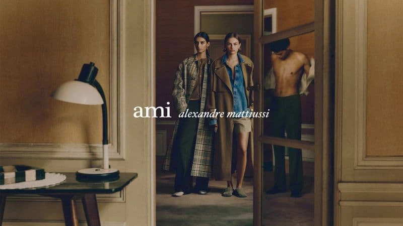 Models in patterned coats standing in a room with a desk lamp in the foreground