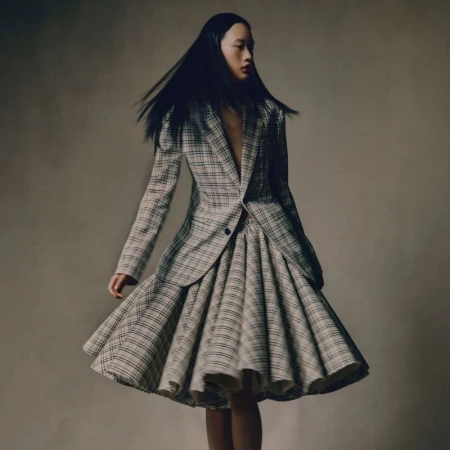 Model with long dark hair wearing a plaid blazer and flared plaid skirt against a neutral background