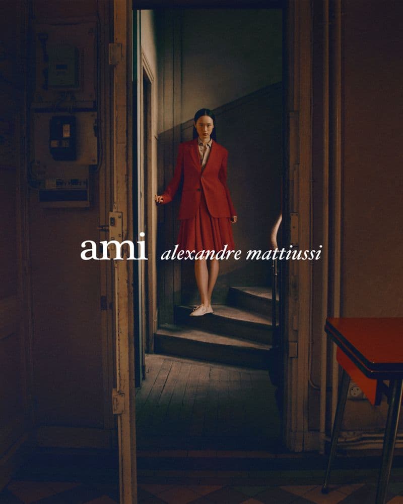 Model standing on a wooden staircase wearing a red suit jacket and matching pleated skirt.