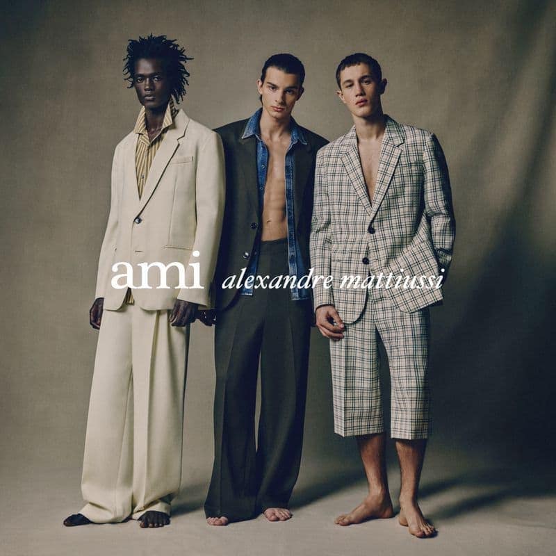 Three male models posing in tailored suits and blazers against a neutral studio backdrop for Ami Paris