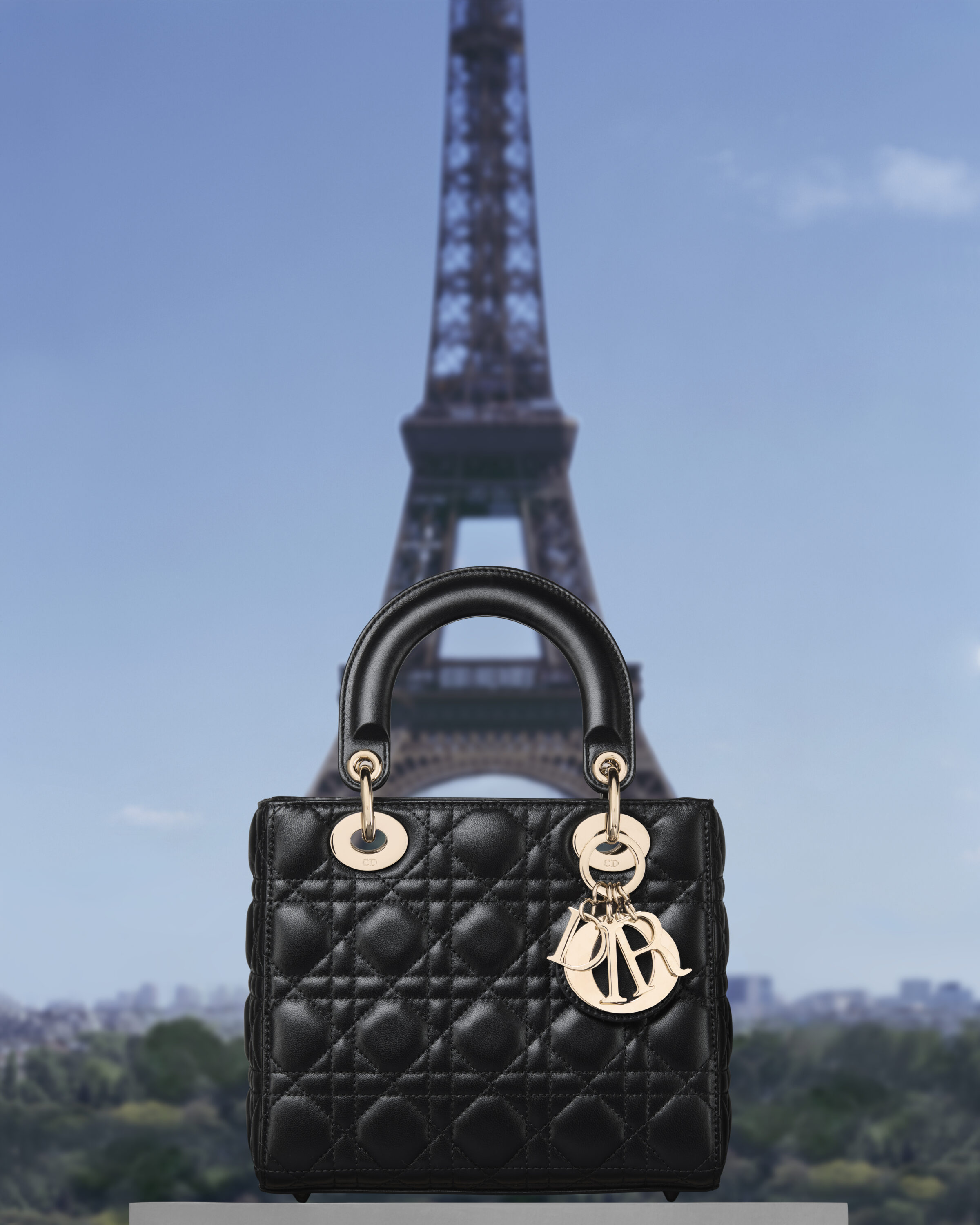 Black quilted leather Dior handbag with gold charms against the Eiffel Tower in Paris.