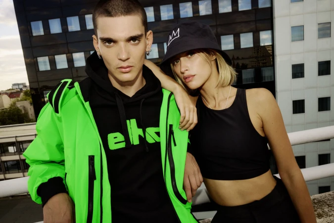Two models wearing black and neon green apparel posing on a rooftop against a modern commercial building exterior