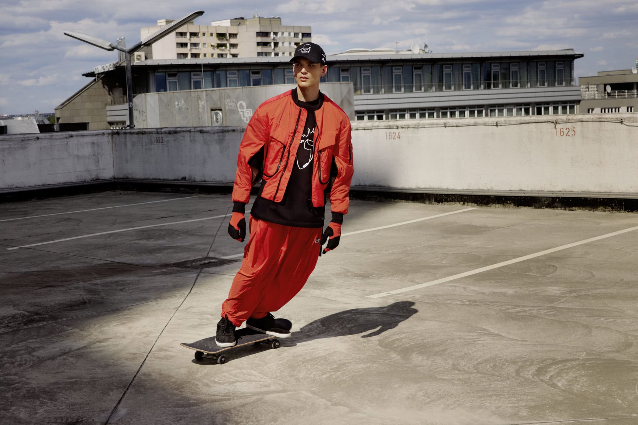 Man wearing a red jacket and red trousers skateboarding on a concrete rooftop under an overcast sky.